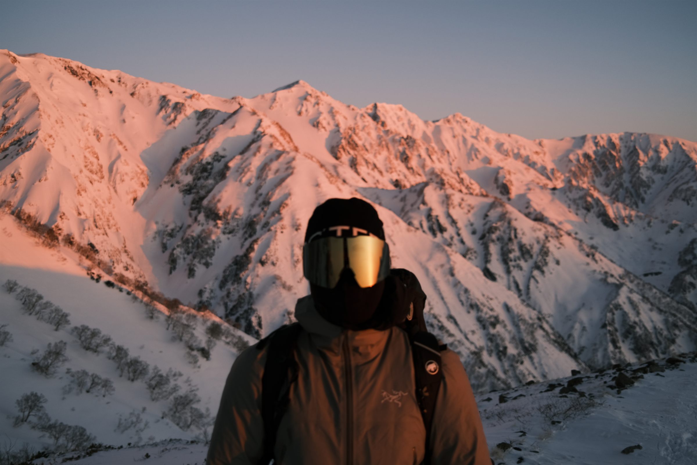 朝焼けに染まる雪山の稜線と、それを背に立つ人物